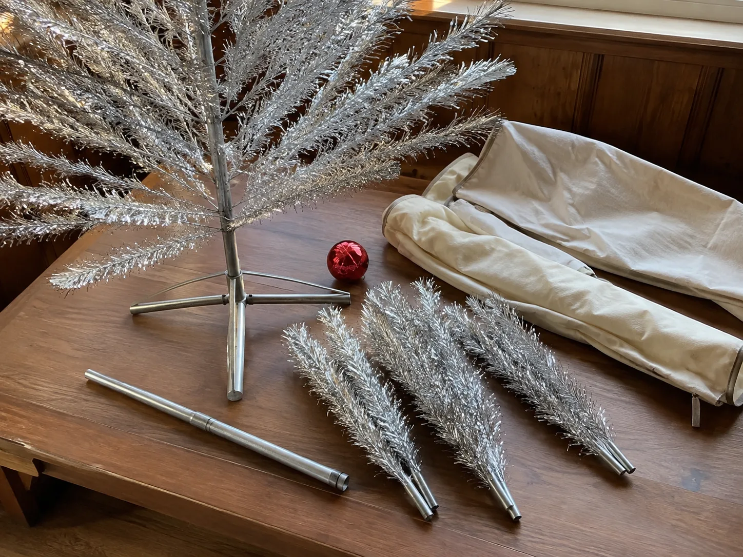 Vintage aluminum Christmas tree branches, stand, and protective storage sleeves arranged for inspection