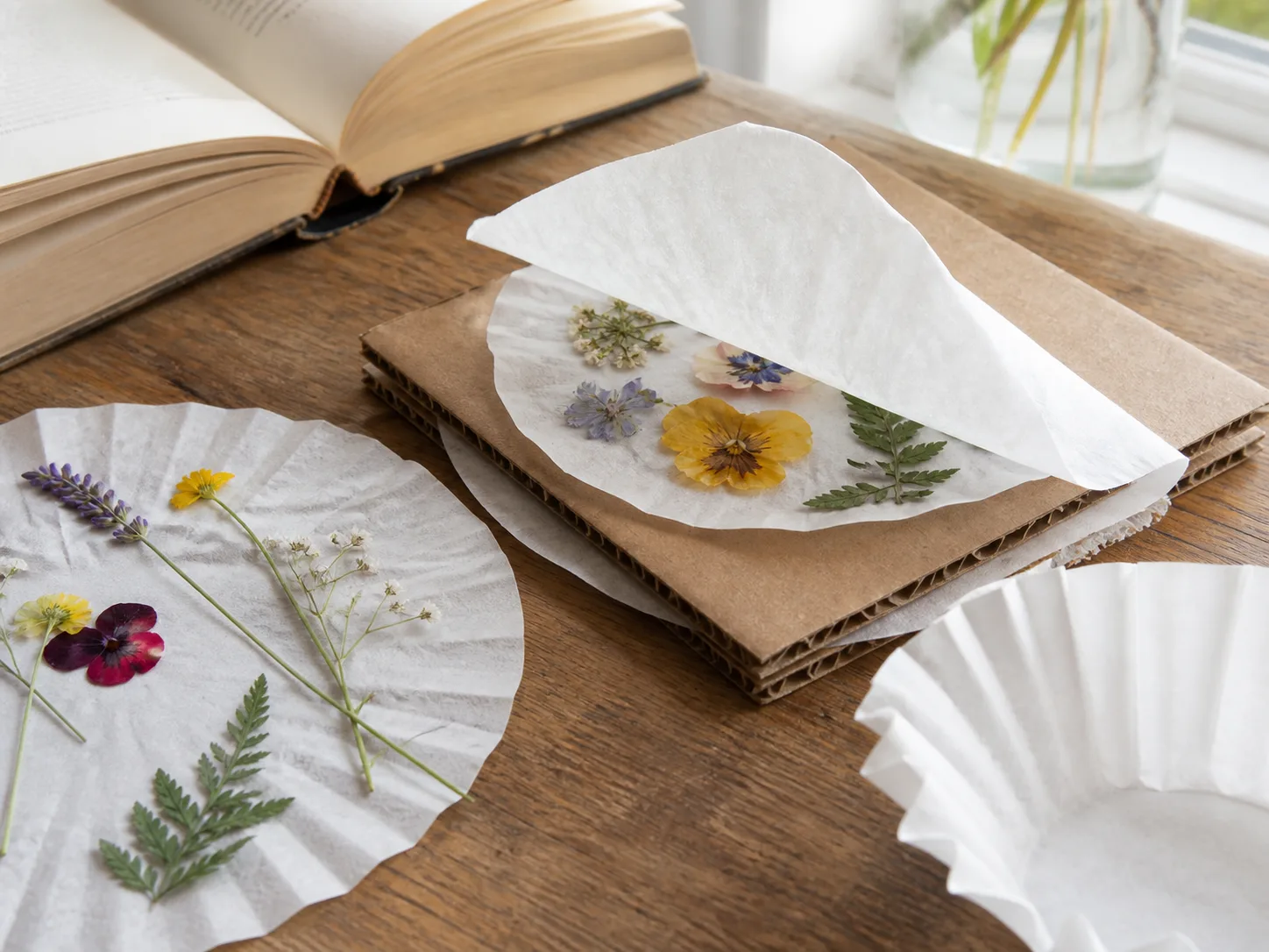 Coffee filters layered with pressed flowers between cardboard on a craft table