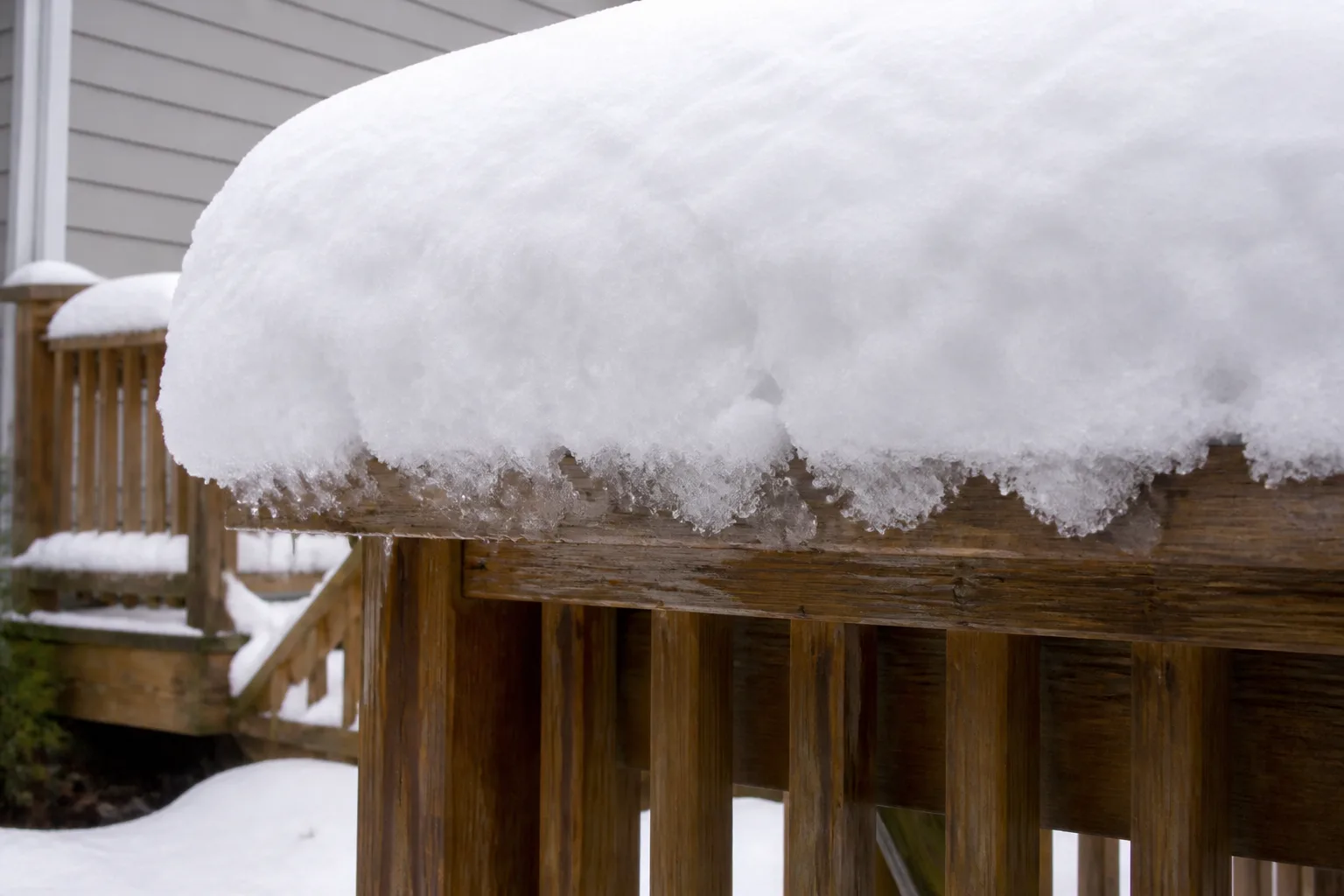 Thick wet heavy snow piled on horizontal wooden deck boards showing snow load on a residential deck