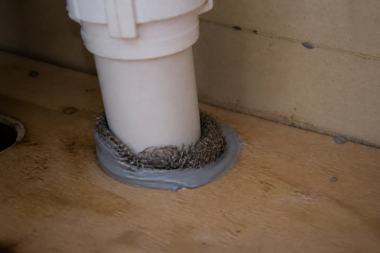 Steel wool packed around a pipe gap under a kitchen sink sealed with caulk
