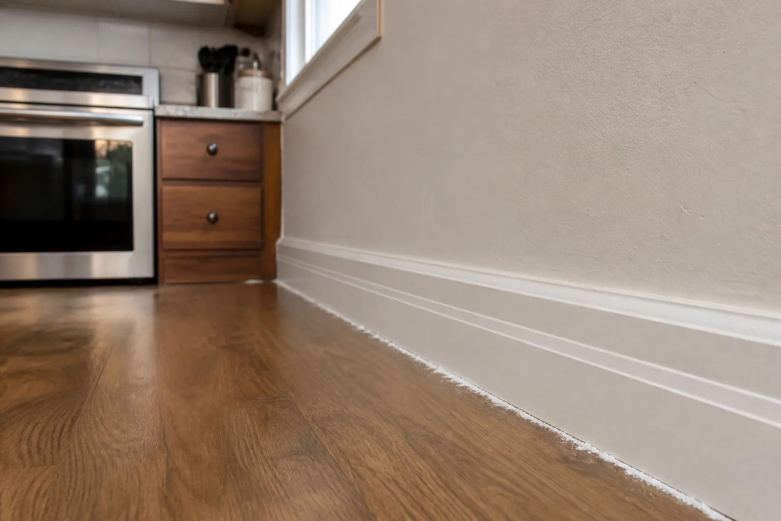 Thin line of white diatomaceous earth powder dusted along a kitchen baseboard crack near the stove