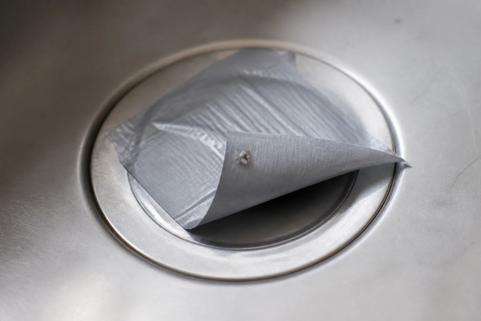 Kitchen sink drain covered with duct tape to trap emerging drain flies during an overnight infestation test