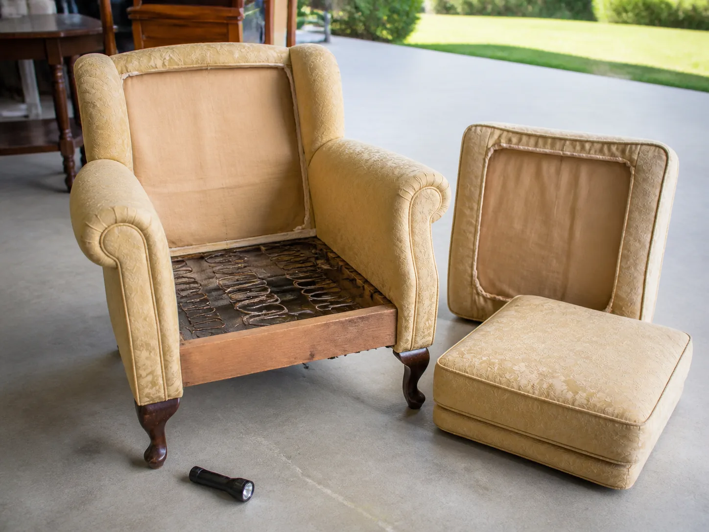 A secondhand upholstered chair with its cushions removed for a close inspection of the seams, frame, and springs
