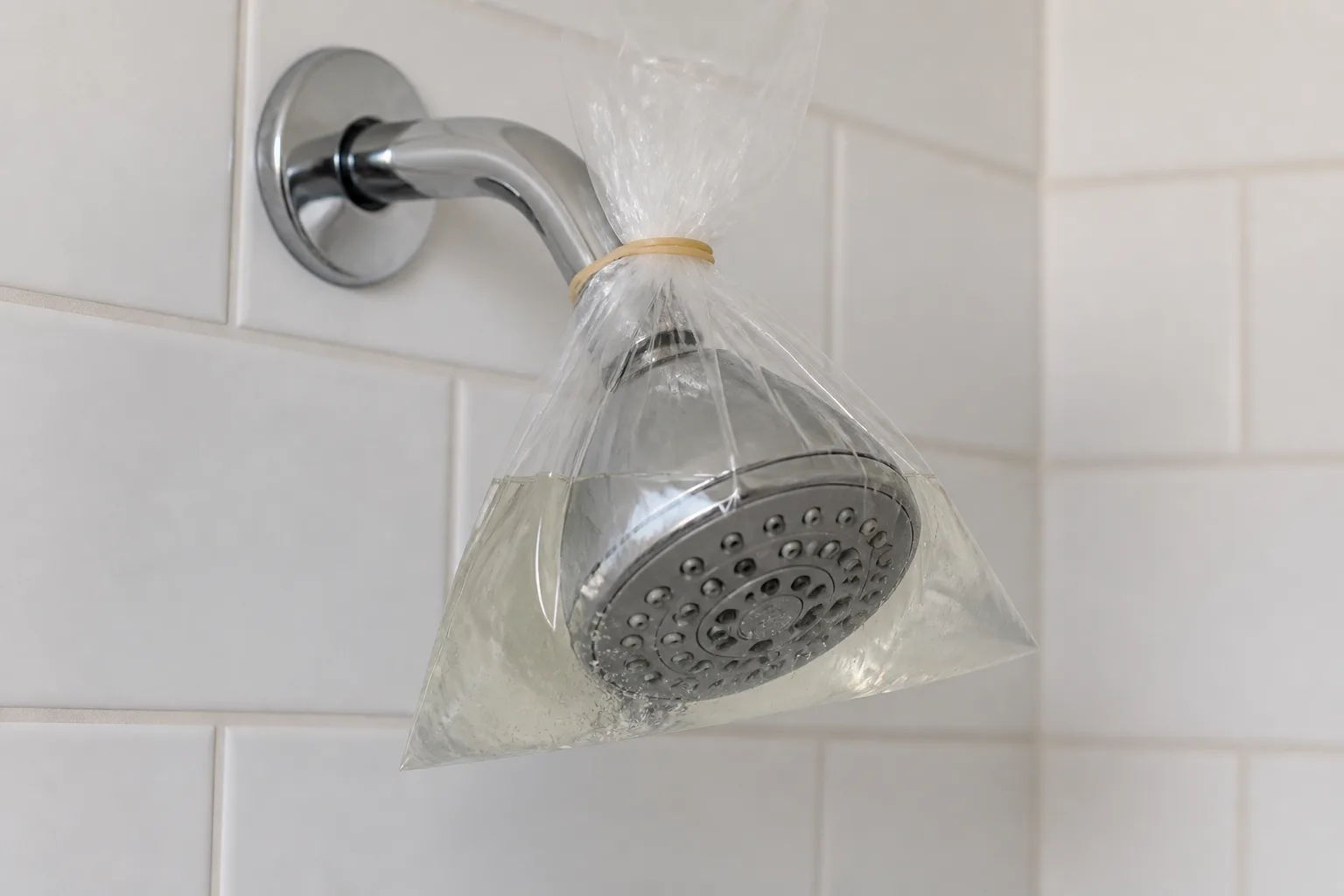 Plastic bag filled with vinegar solution secured over a fixed showerhead with a rubber band for a deep soak