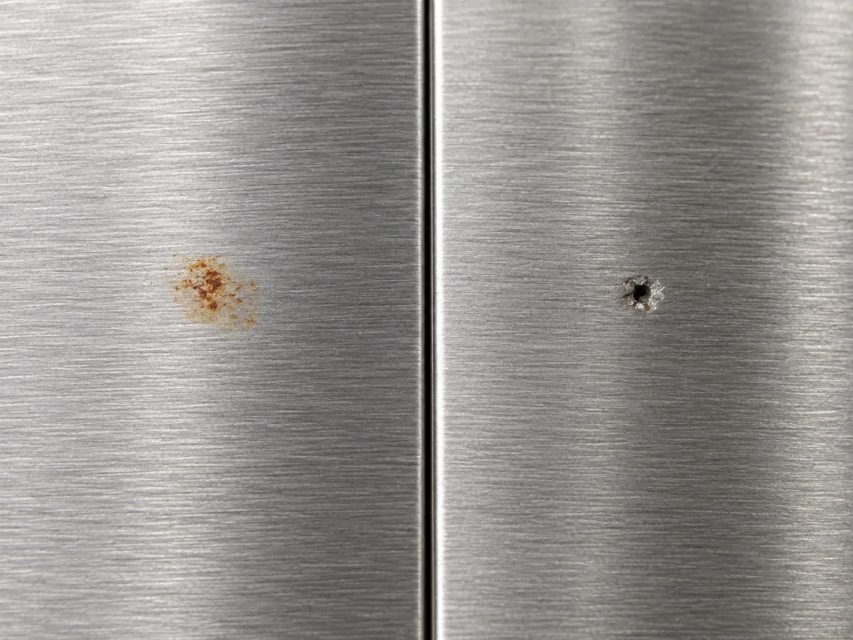 A superficial orange transfer mark and a recessed pit on brushed stainless steel, shown side by side