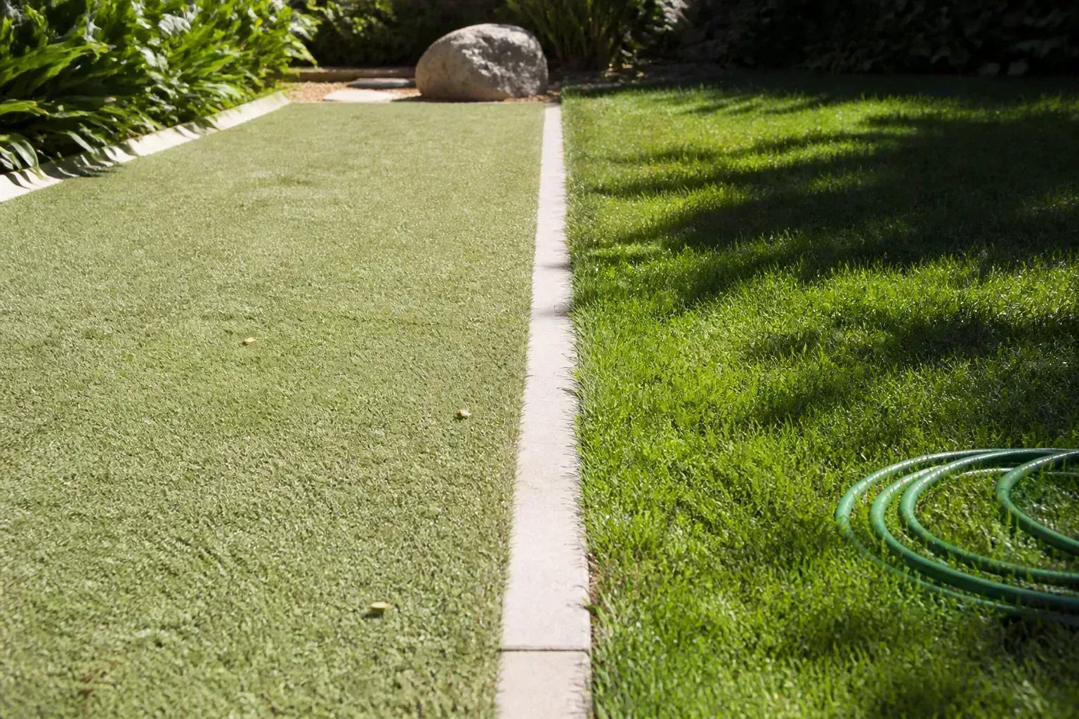 Sun-baked artificial turf beside cooler natural grass in a summer backyard