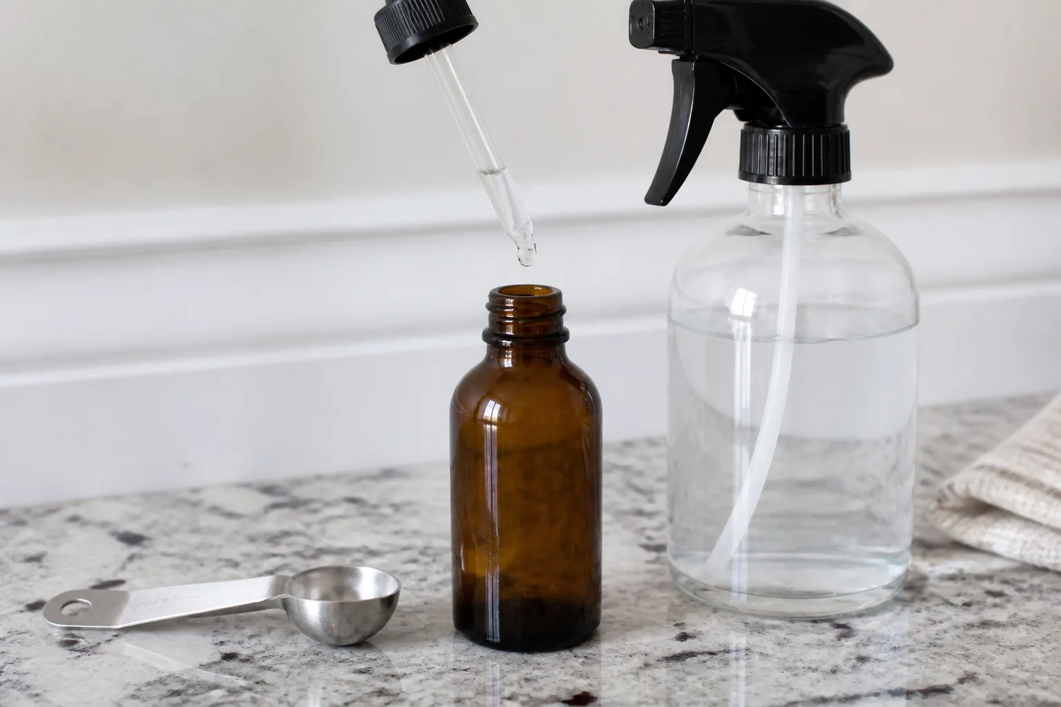 Peppermint essential oil, measuring spoon, and quart spray bottle on a kitchen counter for DIY mouse repellent