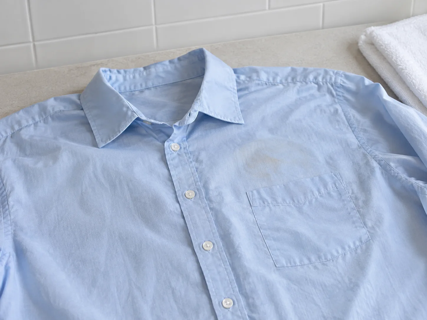 A damp pale-blue shirt laid flat in daylight to check for a remaining coffee mark before machine drying