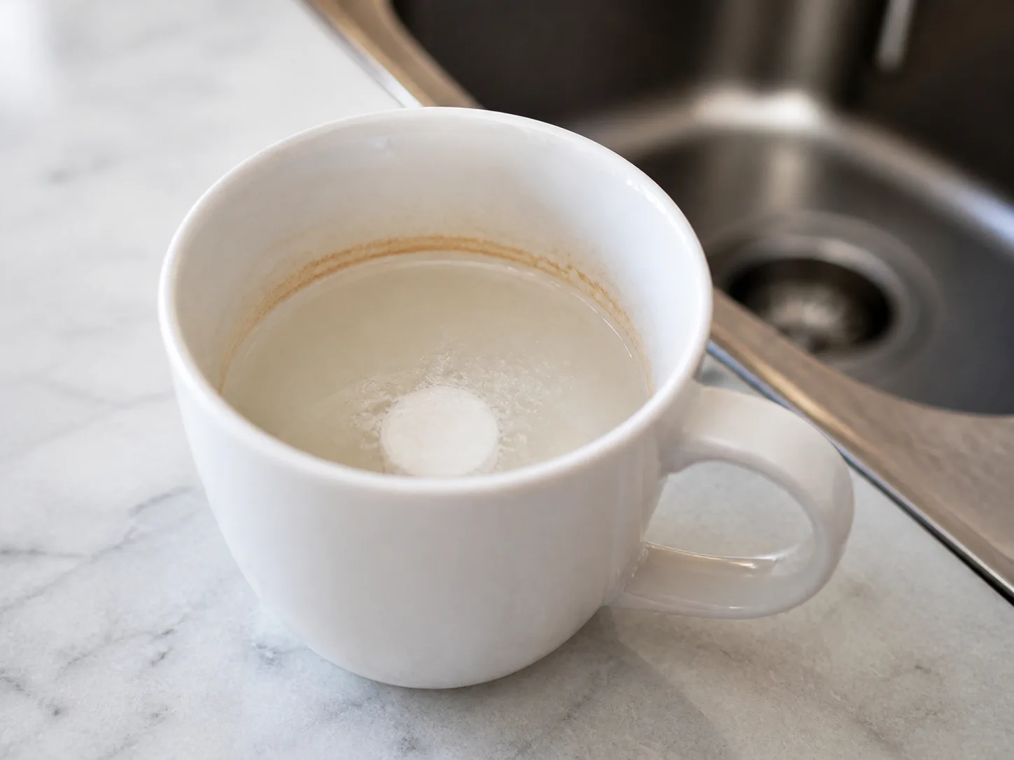 A denture-cleaning tablet fizzing in warm water inside a coffee-stained mug
