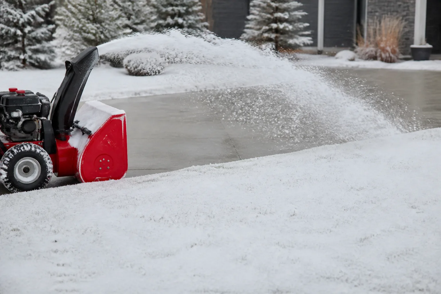 Snow blower clearing a paved driveway beside a lawn
