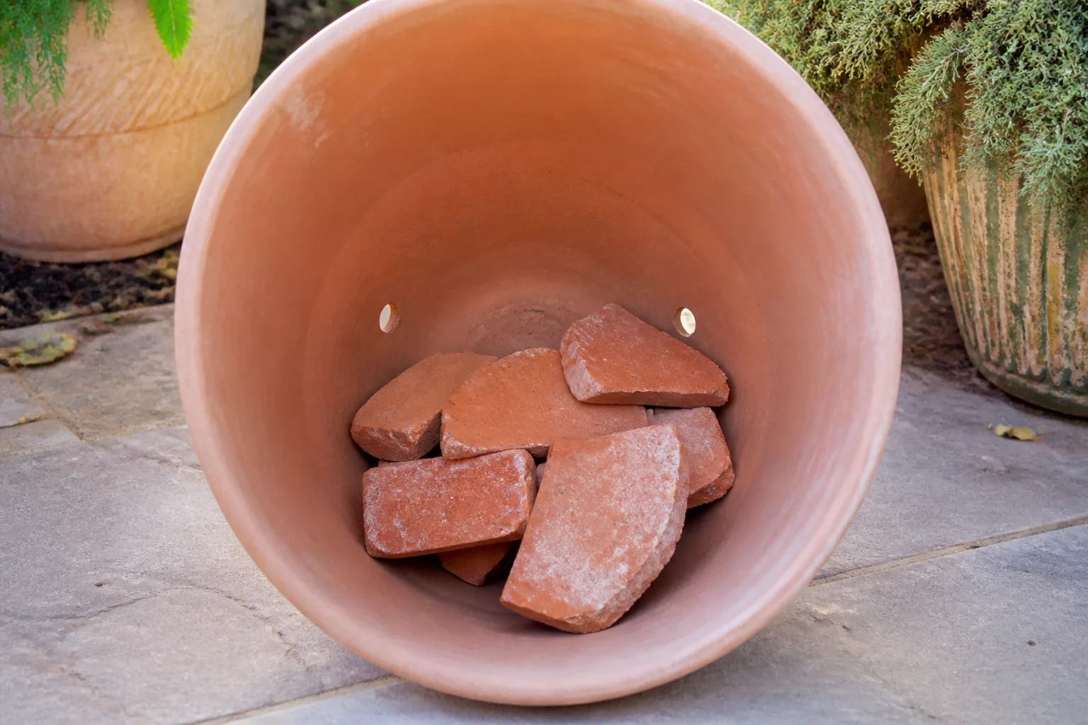 Bricks and large broken terracotta pieces arranged low in the base of a tall planter away from drainage holes